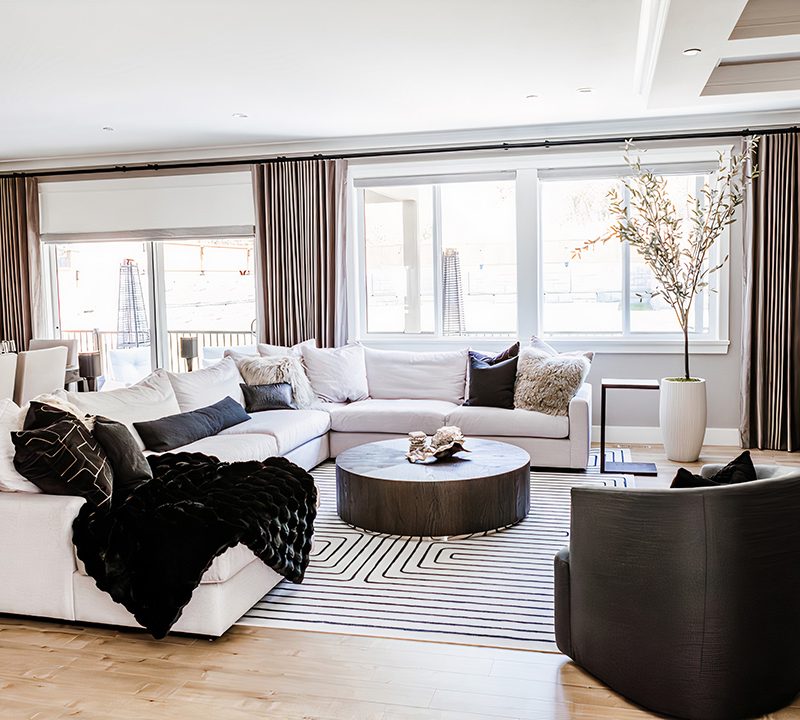 Open plan living room with a pale sectional, round timber coffee table and an olive tree by the windows