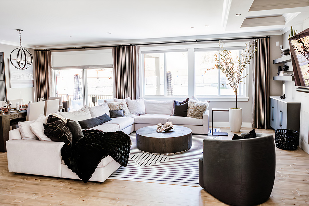 Open plan living room with a pale sectional, round timber coffee table and an olive tree by the windows