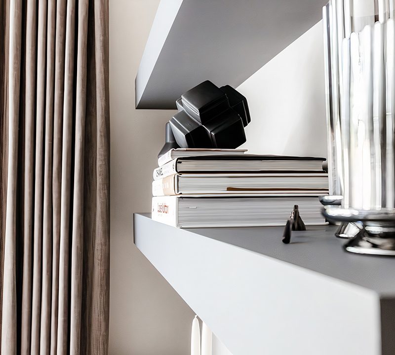 Styled shelf with stacked books, a sculptural black object and a glass vessel