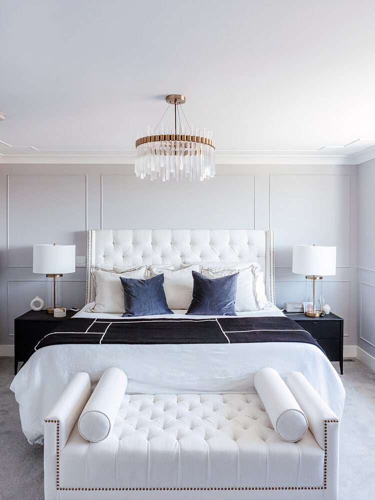 Bedroom with a white tufted headboard, panelled grey walls and a glass and brass chandelier
