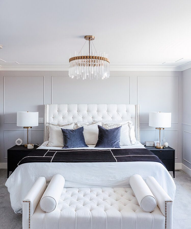 Bedroom with a white tufted headboard, panelled grey walls and a glass and brass chandelier