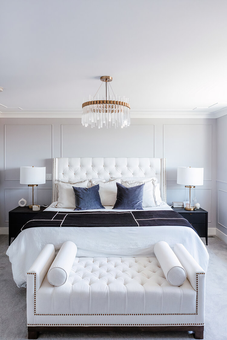 Bedroom with a white tufted headboard, panelled grey walls and a glass and brass chandelier
