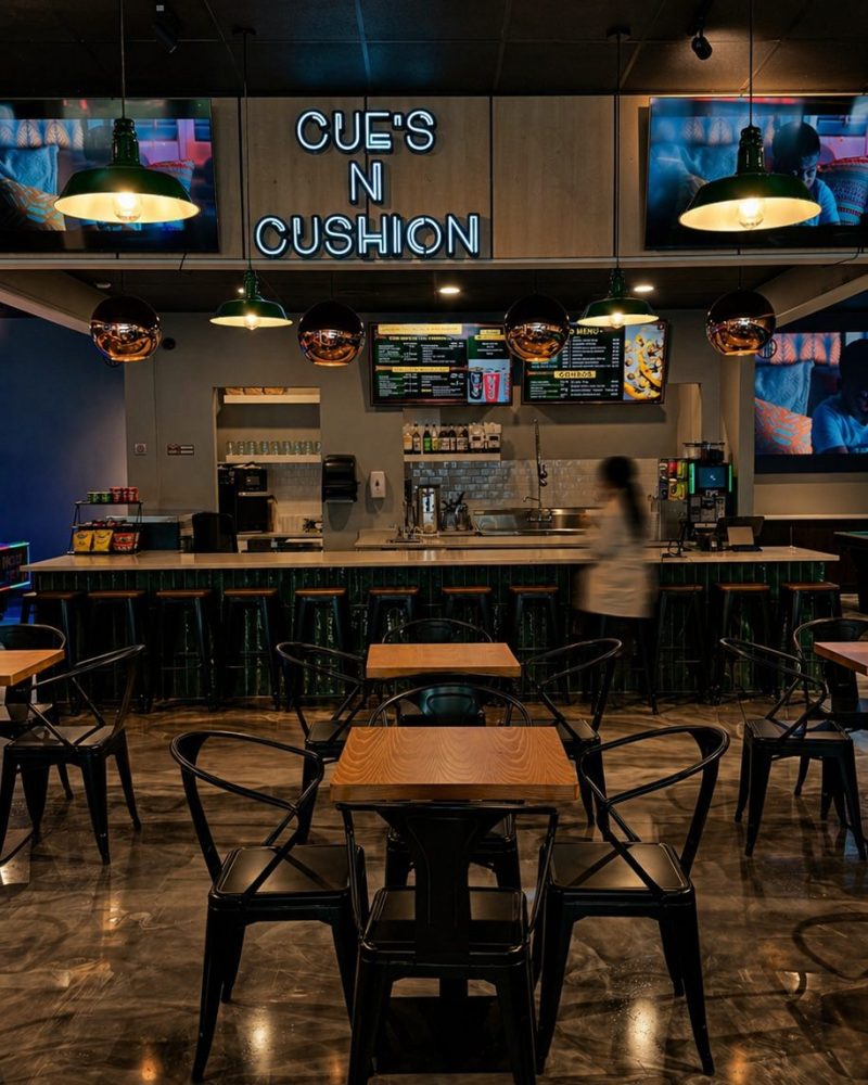 Bar counter with stools and menu screens at Cue's N Cushion