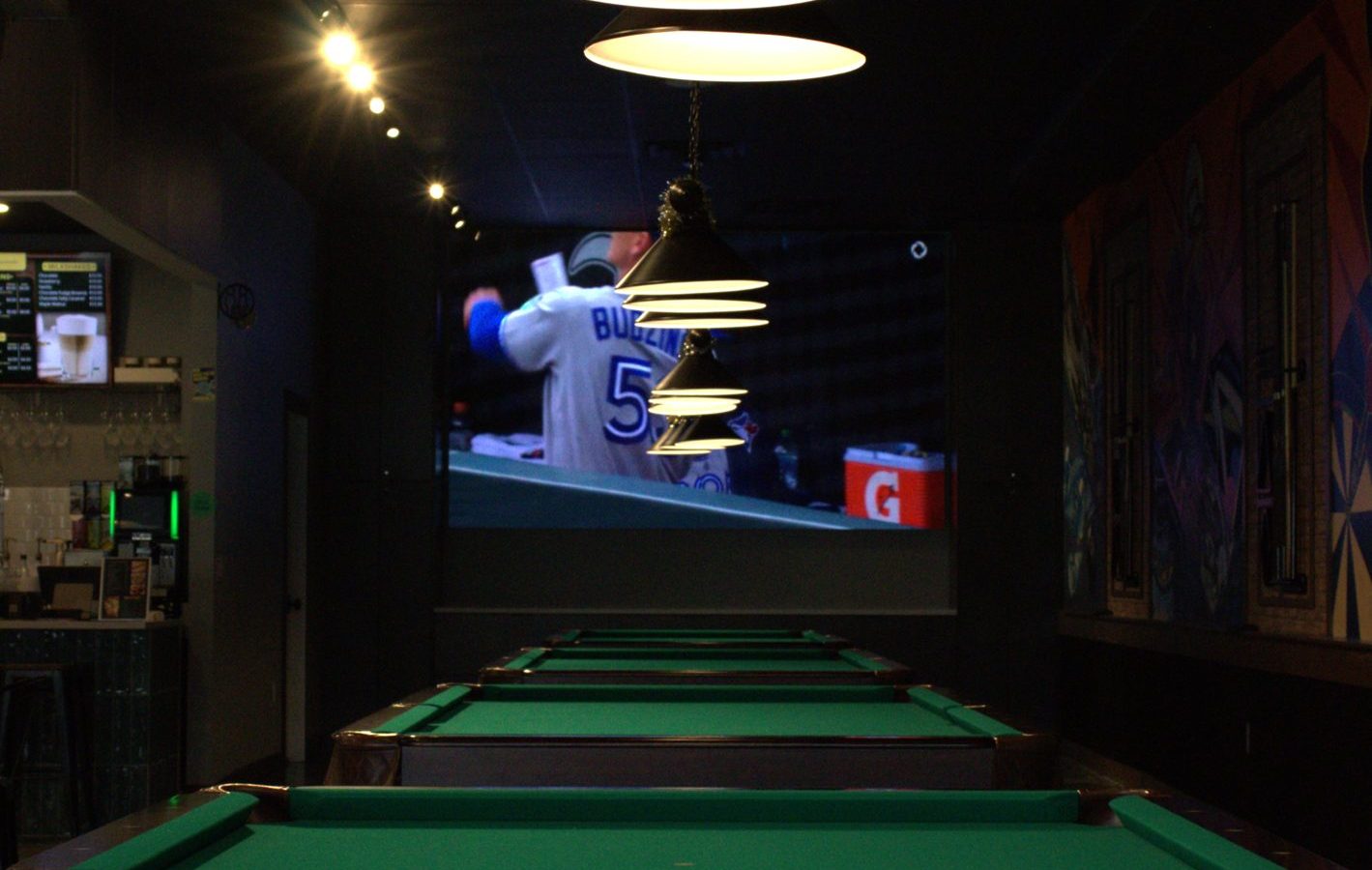 Row of pool tables beneath warm pendant lights at Cue's N Cushion